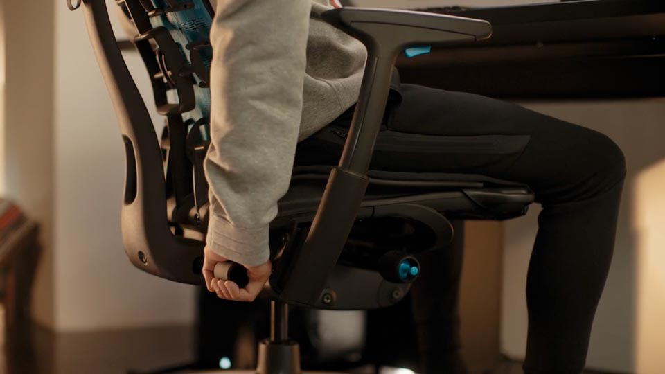 Een video van een persoon die in een zwart-blauwe Embody-gamingstoel van Herman Miller zit en achter de stoel reikt om de rugleuning te verstellen.