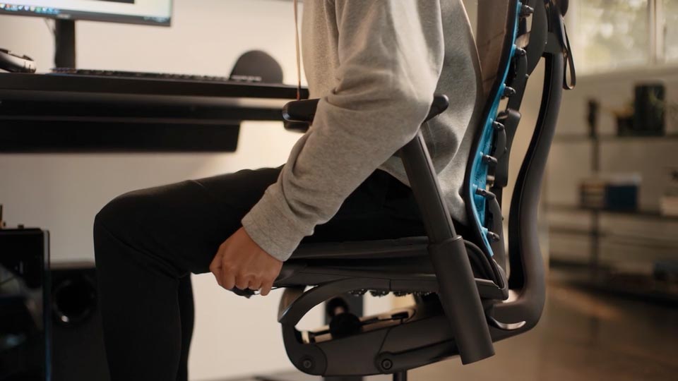 Een video van een persoon die in een zwart-blauwe Embody-gamingstoel van Herman Miller zit en naast de stoel reikt om de zitdiepte aan te passen.