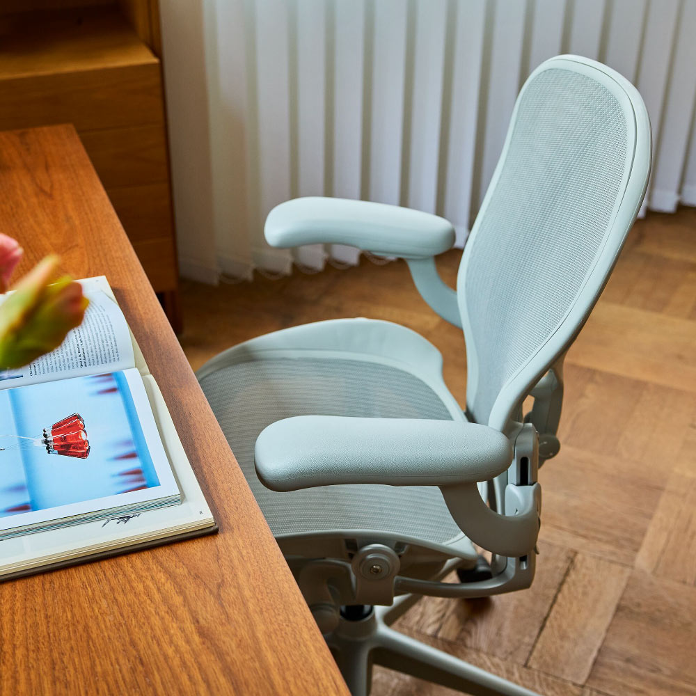 Een lichtgrijze minerale Herman Miller Aeron ergonomische bureaustoel aan een houten tafel.