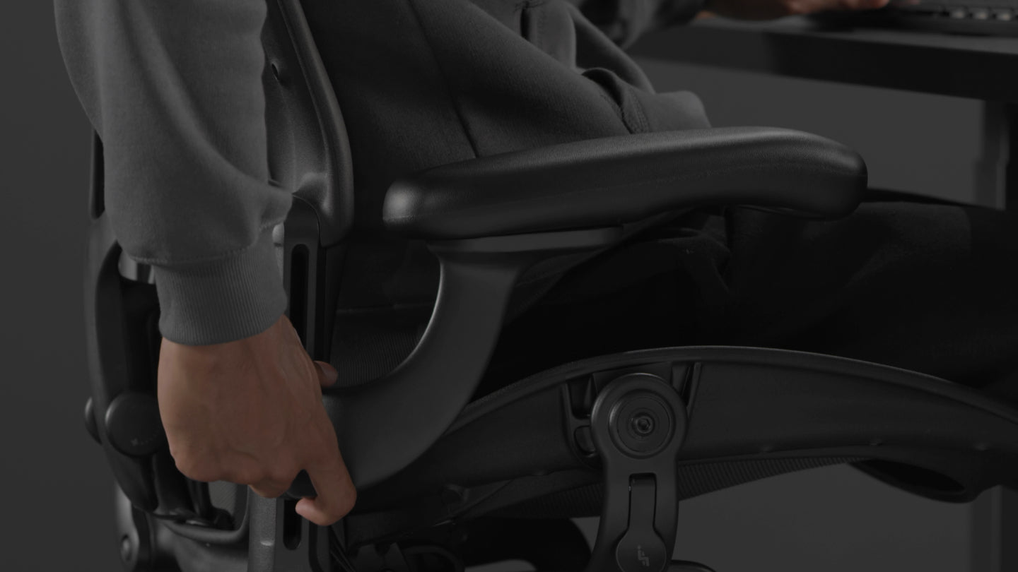 Een video van een persoon die in een zwarte Aeron-gamingstoel van Herman Miller zit en naast de stoel reikt om de armleuningen te verstellen.
