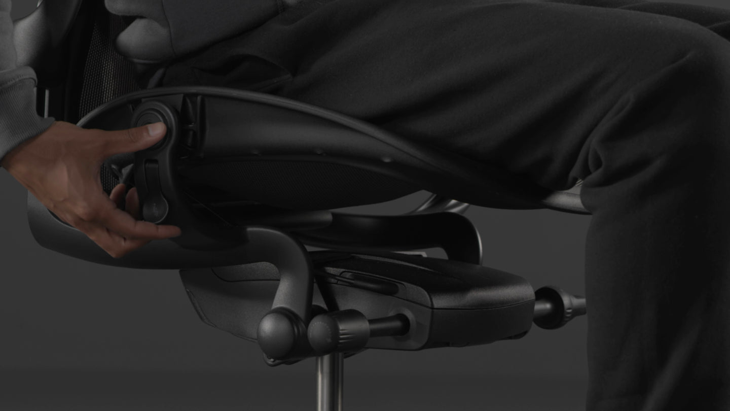 Een video van een persoon die in een zwarte Aeron-gamingstoel van Herman Miller zit en naast de stoel reikt om de zithoogte aan te passen.