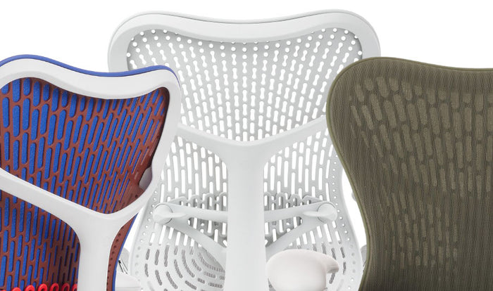 Close-up van drie Mirra 2-bureaustoelen van Herman Miller, met het beschikbare kleurenassortiment. De eerste is blauw, oranje en wit, de tweede is alleen wit en de derde is groen.