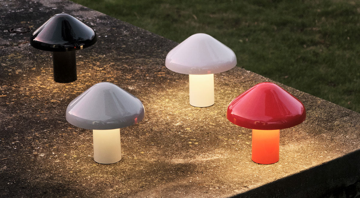 Vier Pao draagbare tafellampen van HAY in zwart, wit, grijs en rood. Buiten in een tuin geplaatst, verspreiden ze een zachte, warme gloed.