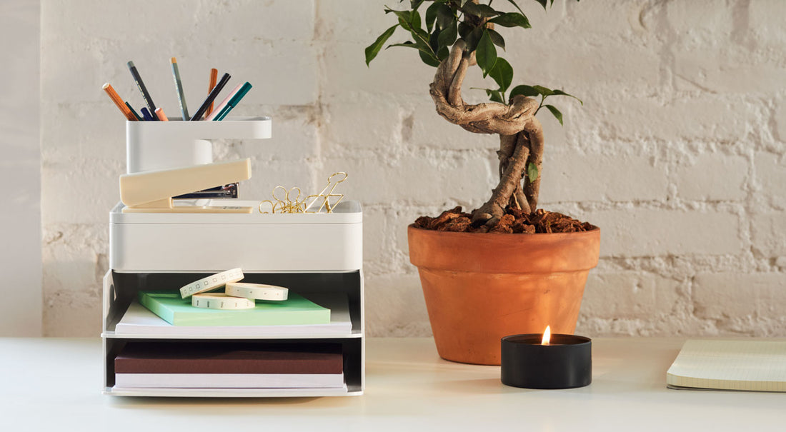 Een set betongrijze Formwork-bureauaccessoires naast een plant en kaars op een bureau.