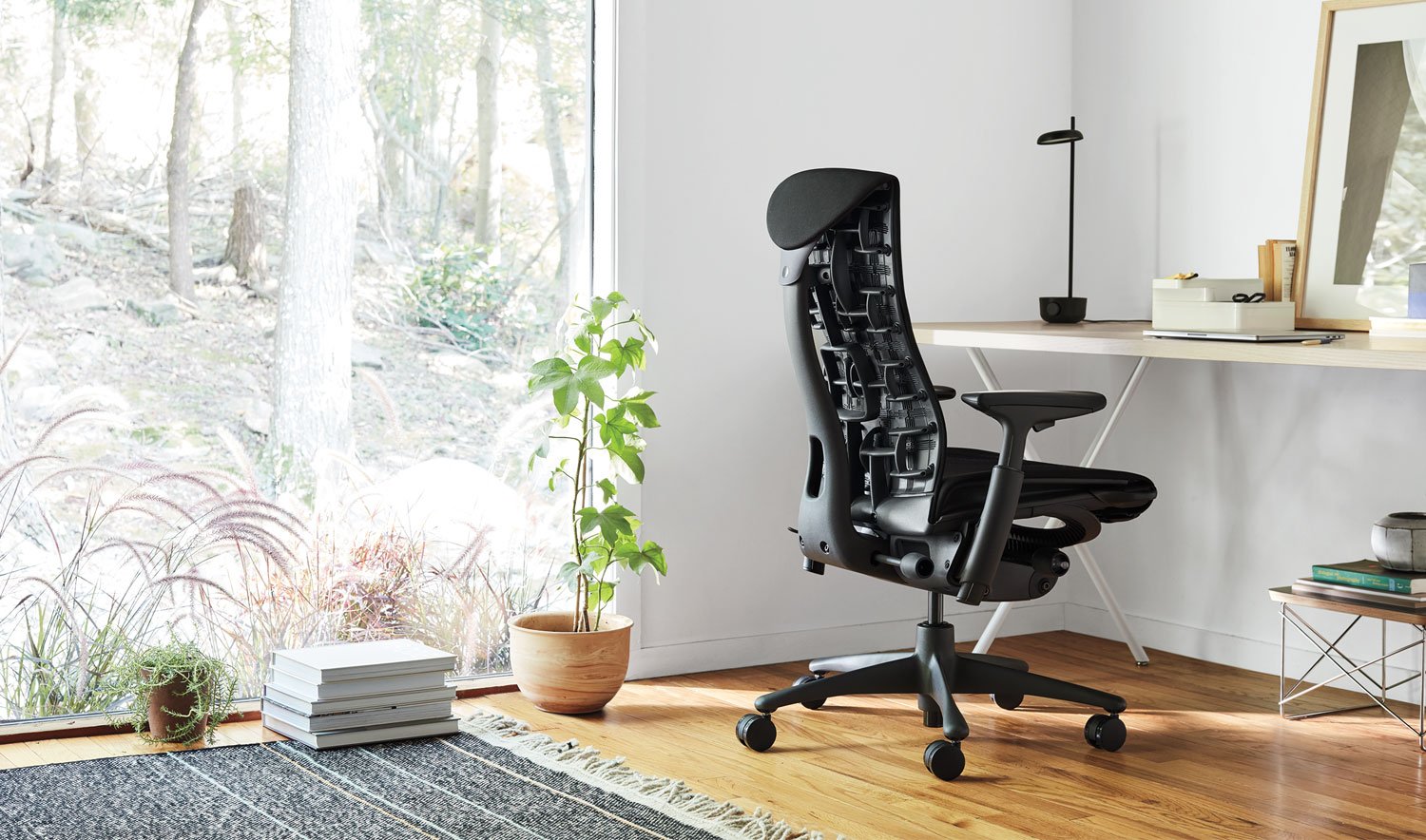 Een zwarte Embody-bureaustoel van Herman Miller, geplaatst in een binnenomgeving. De ruimte bevat elementen zoals meubilair, vloerbedekking en decoratieve items zoals een bloempot en vaas.