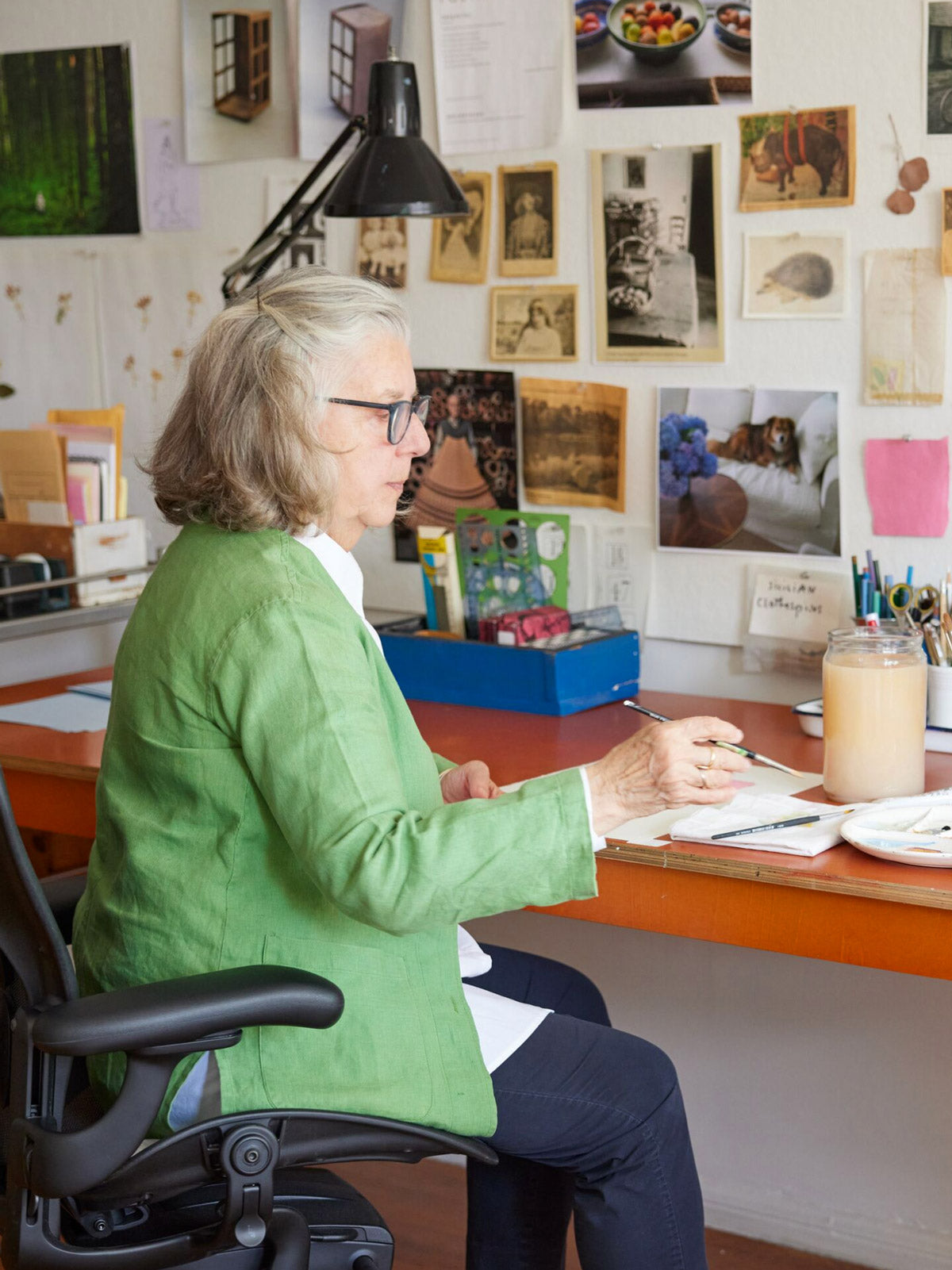 Foto van illustrator, schilder en auteur zittend aan een bureau, schilderend in een Aerong-bureaustoel in grafiet