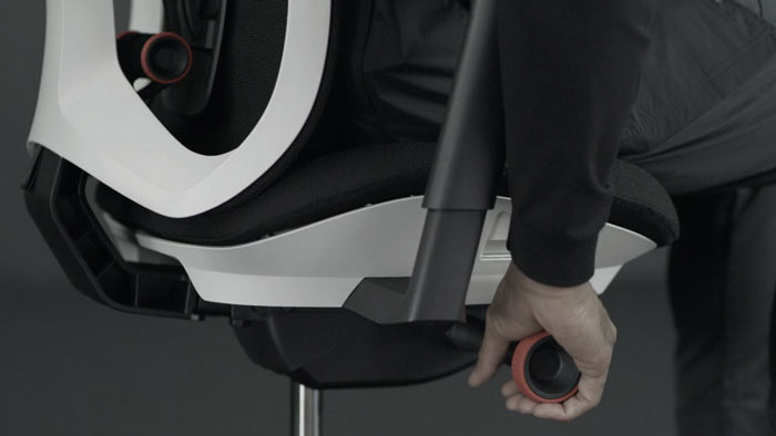 Een video van een persoon die in een wit-zwarte Vantum-gamingstoel van Herman Miller zit en naast de stoel reikt om de kantelspanning aan te passen.