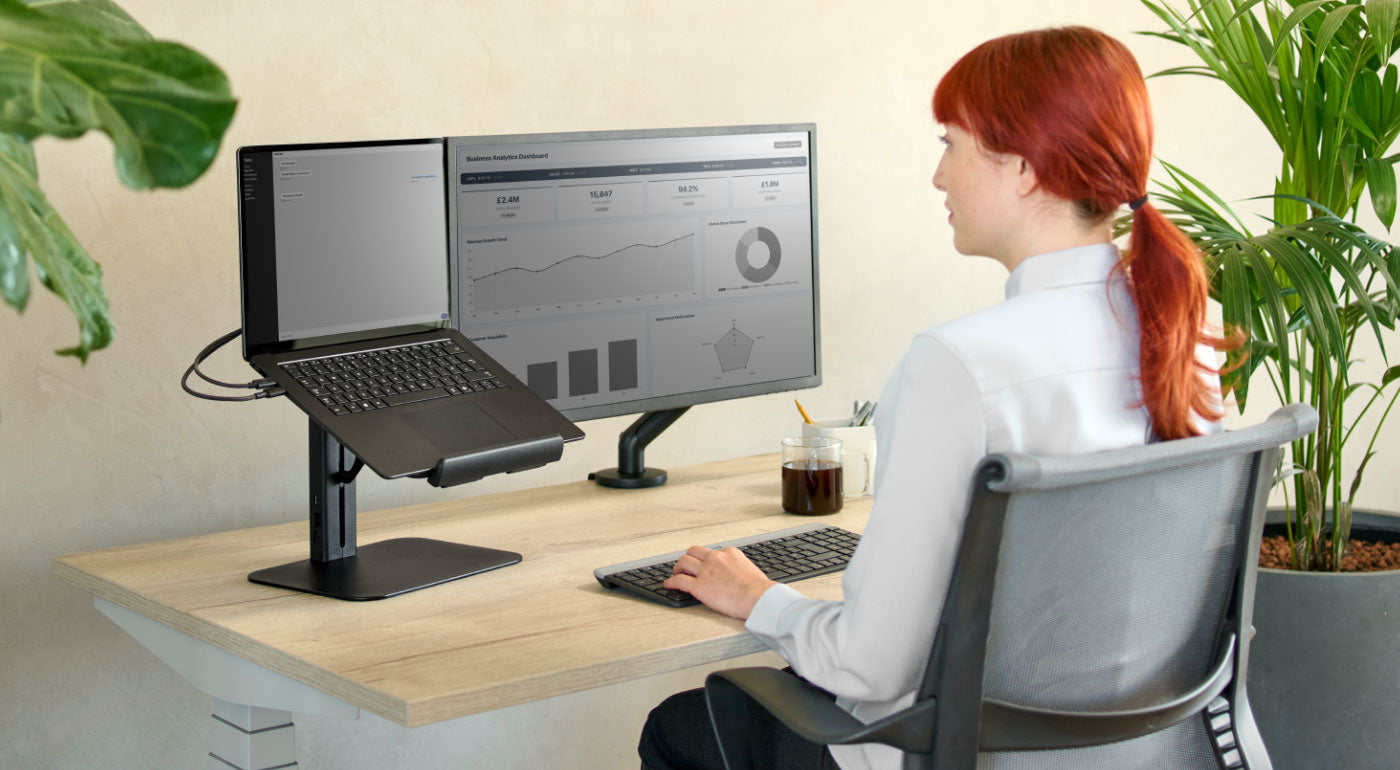 Een dame die een thuiskantooropstelling gebruikt met een Nevi-bureau, Setu-stoel en Lana-laptopstandaard.