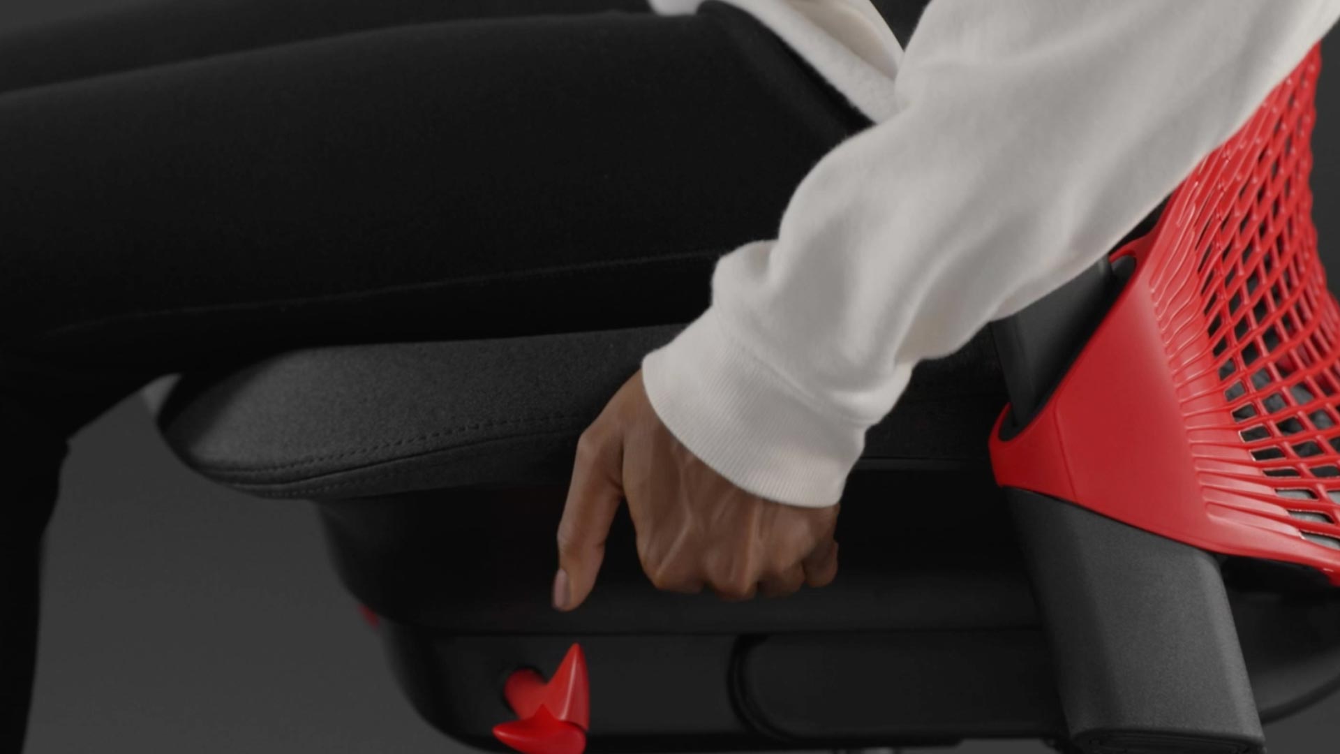 Een video van een persoon die in een rood-zwarte Sayl-gamingstoel van Herman Miller zit en naast de stoel reikt om de zitdiepte aan te passen.
