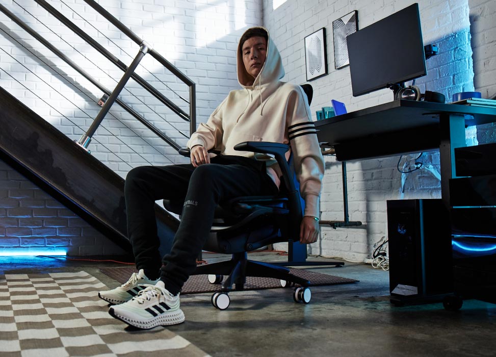 Foto van Jelty van het G2 Esports-team, zittend in een G2 Embody-stoel met zijn rug naar de gamingopstelling, inclusief een Nevi-gamingbureau in zwart met Ollin-monitoren