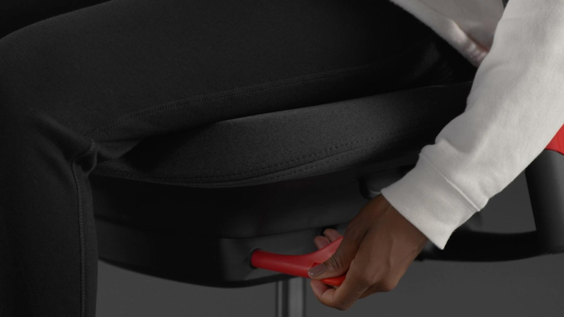 Een video van een persoon die in een rood-zwarte Sayl-gamingstoel van Herman Miller zit en naast de stoel reikt om de voorwaartse kanteling aan te passen.