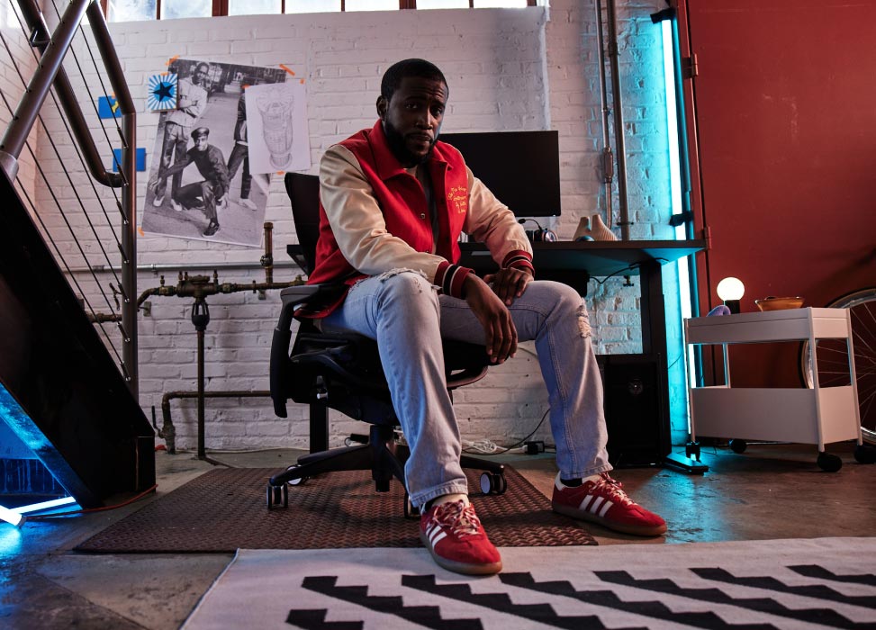 Foto van Deansocool van het G2 Esports-team, zittend in een G2 Embody-stoel met zijn rug naar de gamingopstelling, inclusief een zwarte Nevi-gamingtafel met Ollin-monitoren