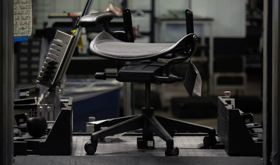Onderstel en zitting van een zwarte Aeron-gamingstoel van Herman Miller in een fabrieksomgeving.