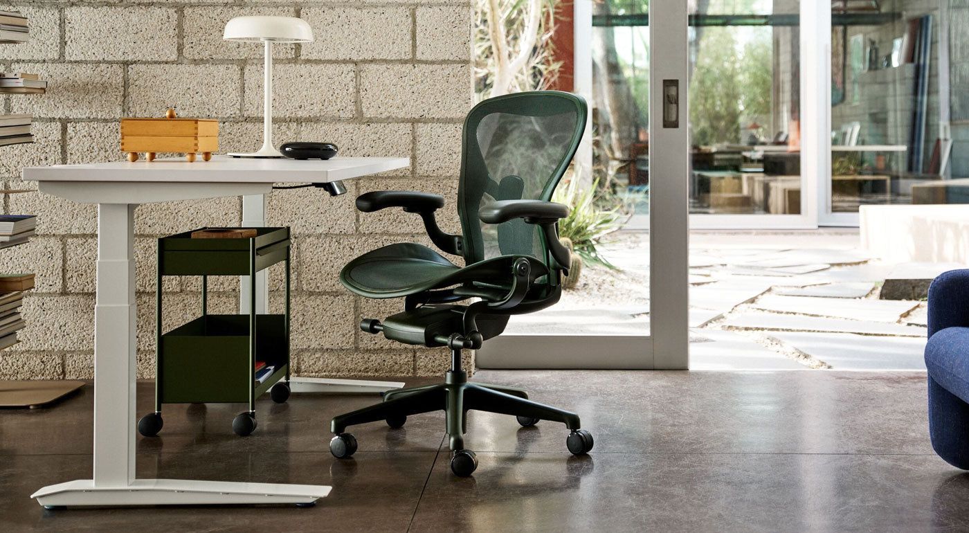 Een Herman Miller Aeron-bureaustoel in Jasper groen als onderdeel van een licht huiskantoor met een wit Jarvis zit-sta-bureau en een olijfgroene OE1-opbergkar.