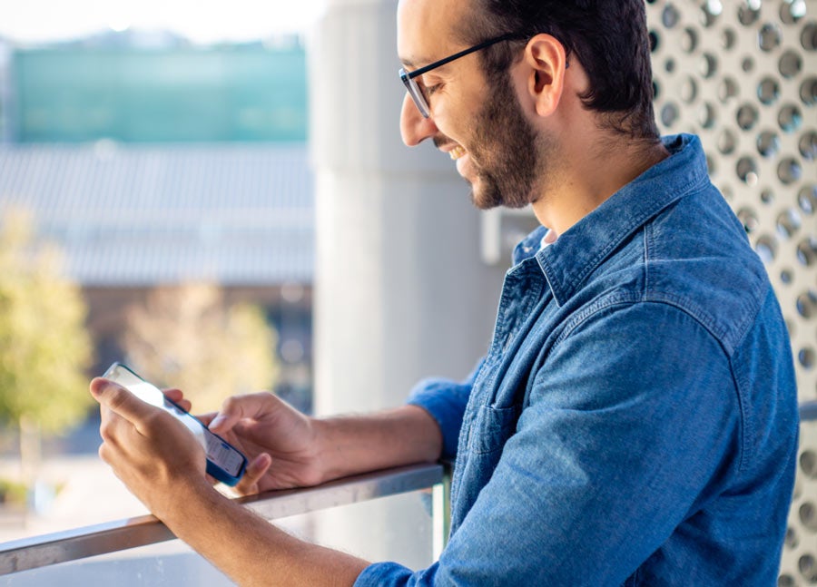 Foto van Ali Abdaal bij het raam in zijn huis, kijkend naar zijn telefoon