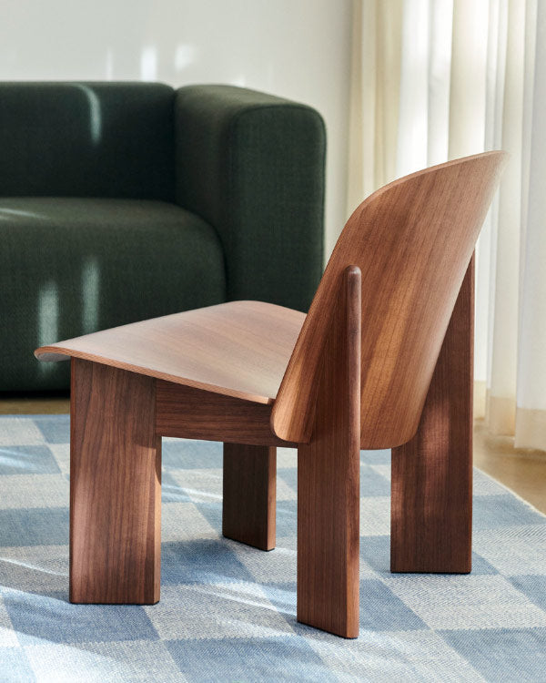 Achteraanzicht van een walnoothouten Chisel-fauteuil van HAY, geplaatst in een binnenruimte op een blauw geruit tapijt.