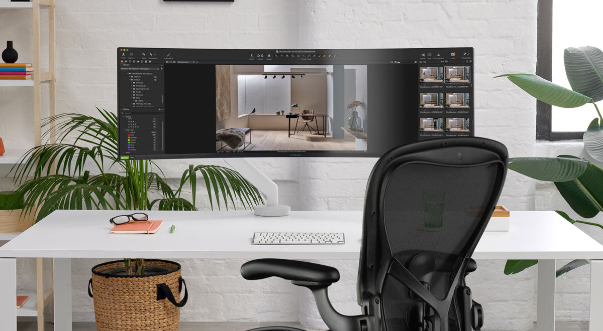 Vooraanzicht van een witte Flo X-monitorarm van CBS bevestigd aan een wit bureau, geplaatst voor een zwarte Aeron-bureaustoel van Herman Miller.