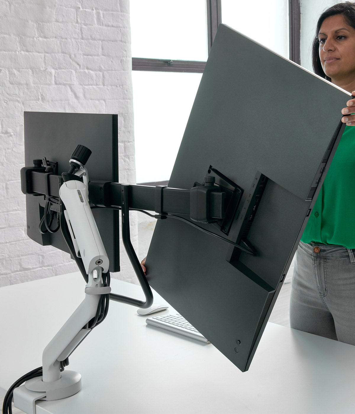 Een CBS Flo X-monitorarm voor grote schermen waarop twee beeldschermen zijn bevestigd, terwijl een gebruiker de stand aanpast.