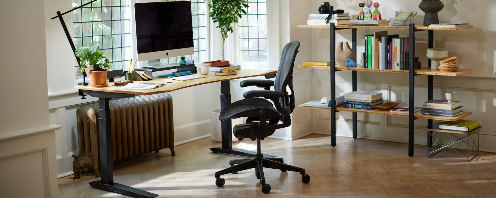 Thuiskantoor met iconische Herman Miller Aeron-stoel in onyxzwart met Jarvis-sta- en zitbureau met poten en gebogen bamboe blad.