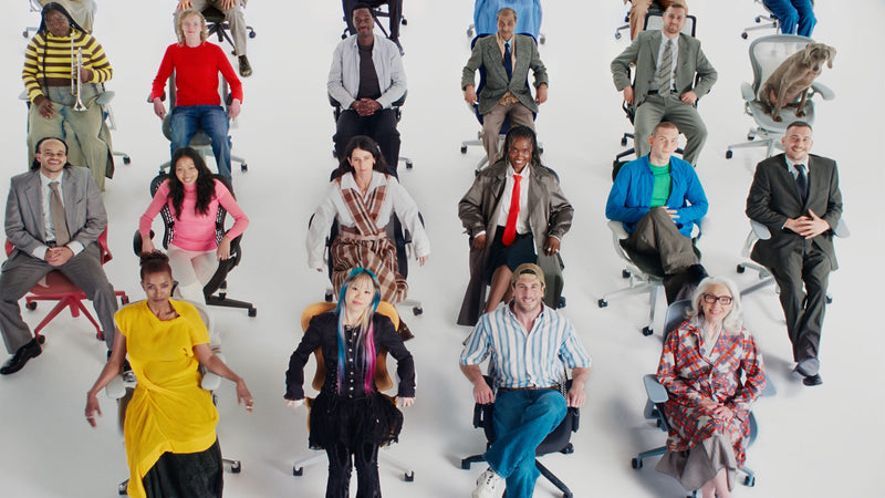 Een grote, diverse groep mensen zat op een selectie van ergonomische bureaustoelen van Herman Miller in een witte studio-omgeving.