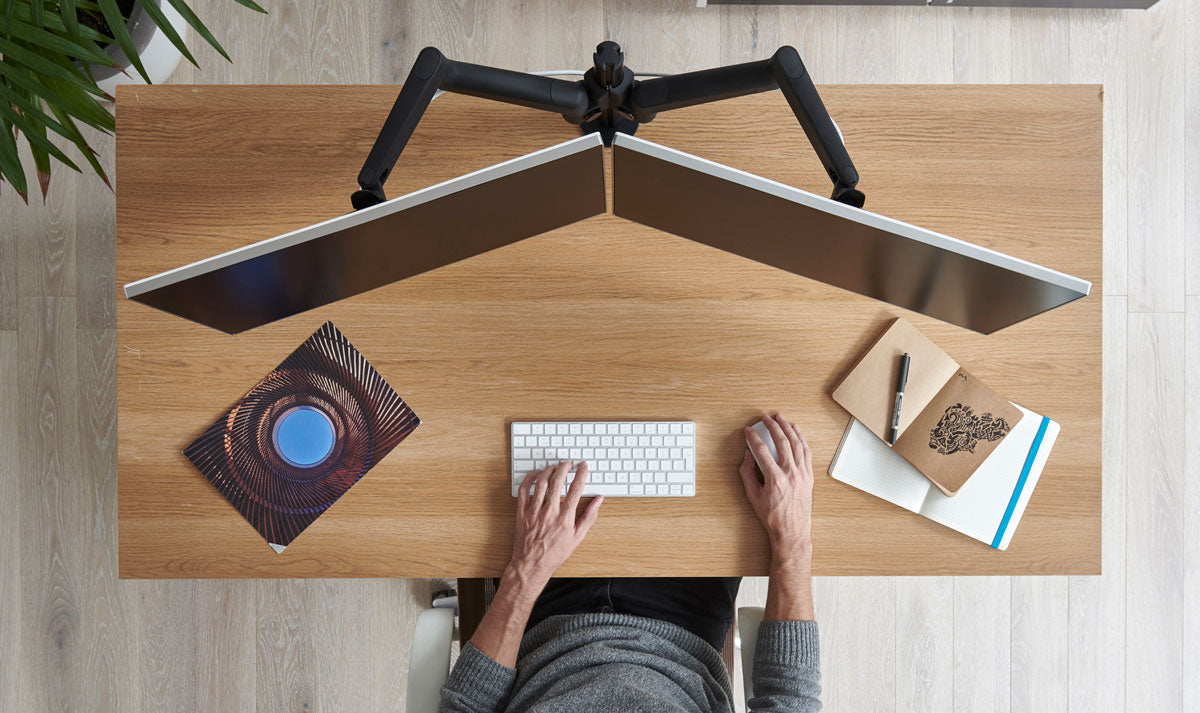 Bovenaanzicht van een houten bureau met een dubbele monitorarm van Lima waarop twee schermen zijn bevestigd.