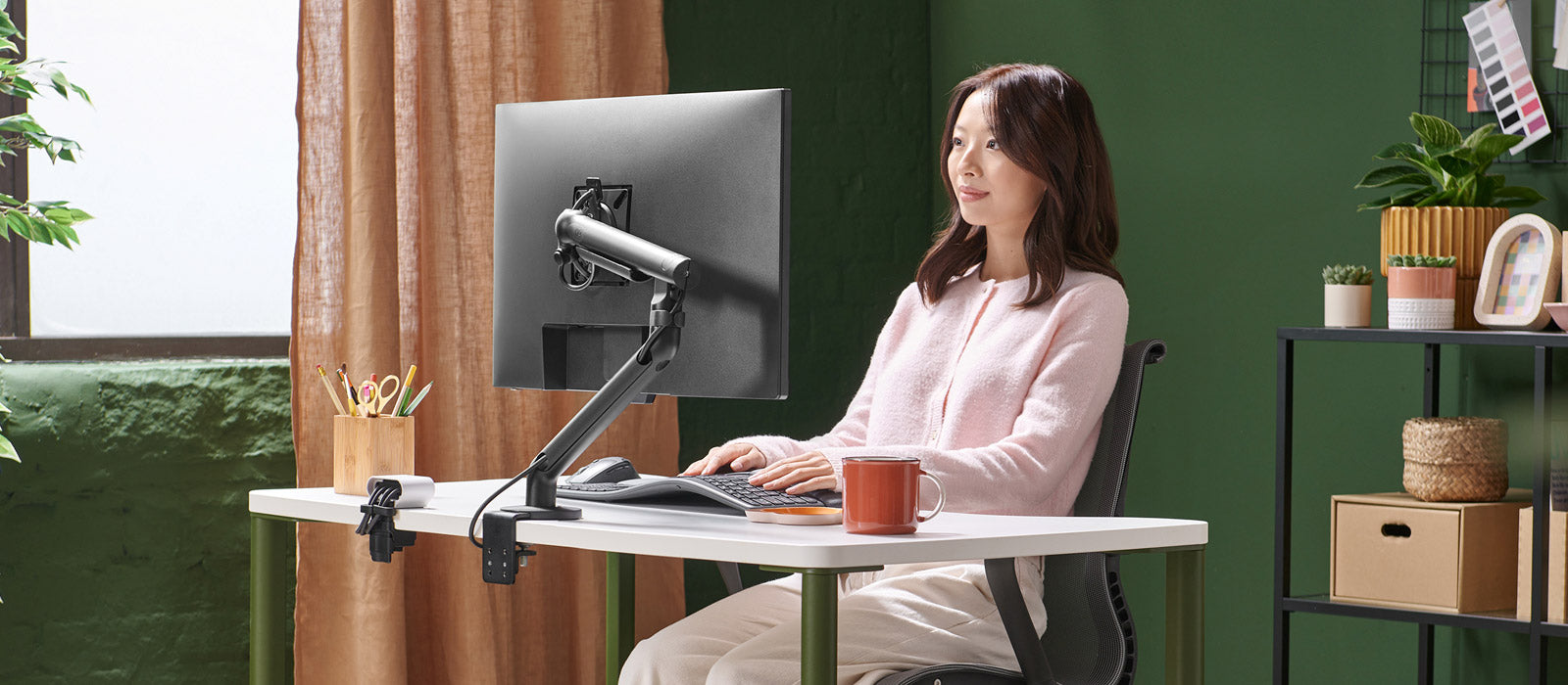Een vrouw zat aan een Herman Miller OE1-bureau te werken achter een beeldscherm dat werd ondersteund door een zwarte Flo-monitorarm.