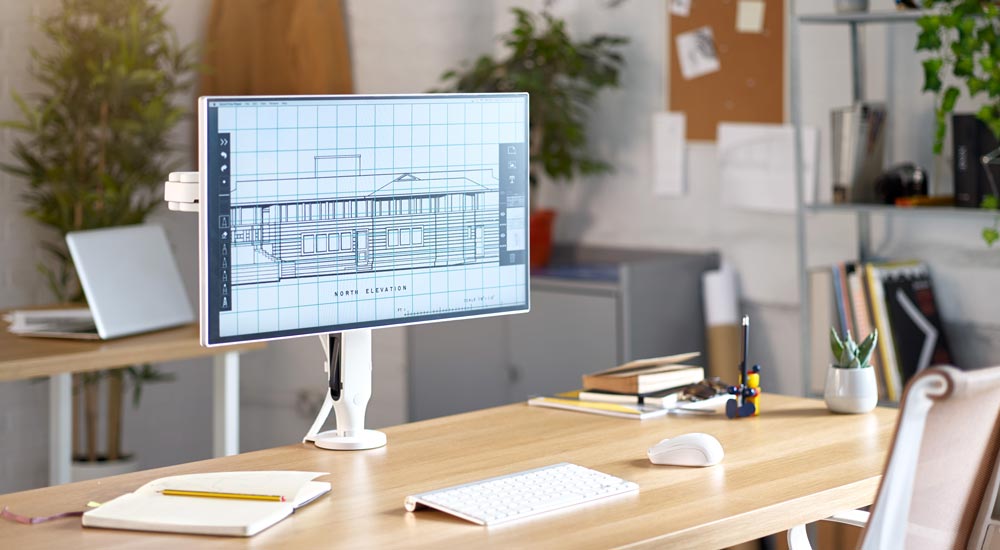 Een witte Ollin-monitorarm van CBS, gemonteerd op een houten bureau met een computerscherm, geplaatst in een kantooromgeving.