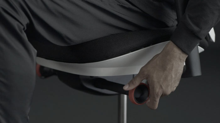 Een video van een persoon die in een wit-zwarte Vantum-gamingstoel van Herman Miller zit en naast de stoel reikt om de kantelbeveiliging aan te passen.
