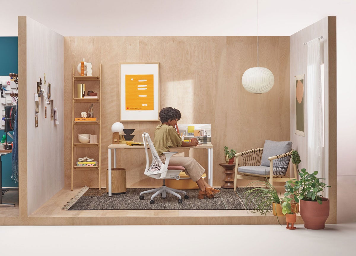 Vrouw zit aan een bureau in een neutraal thuiskantoor met een Sayl-bureaustoel in wit voor een OE1-bureau met witte poten en een licht houten blad