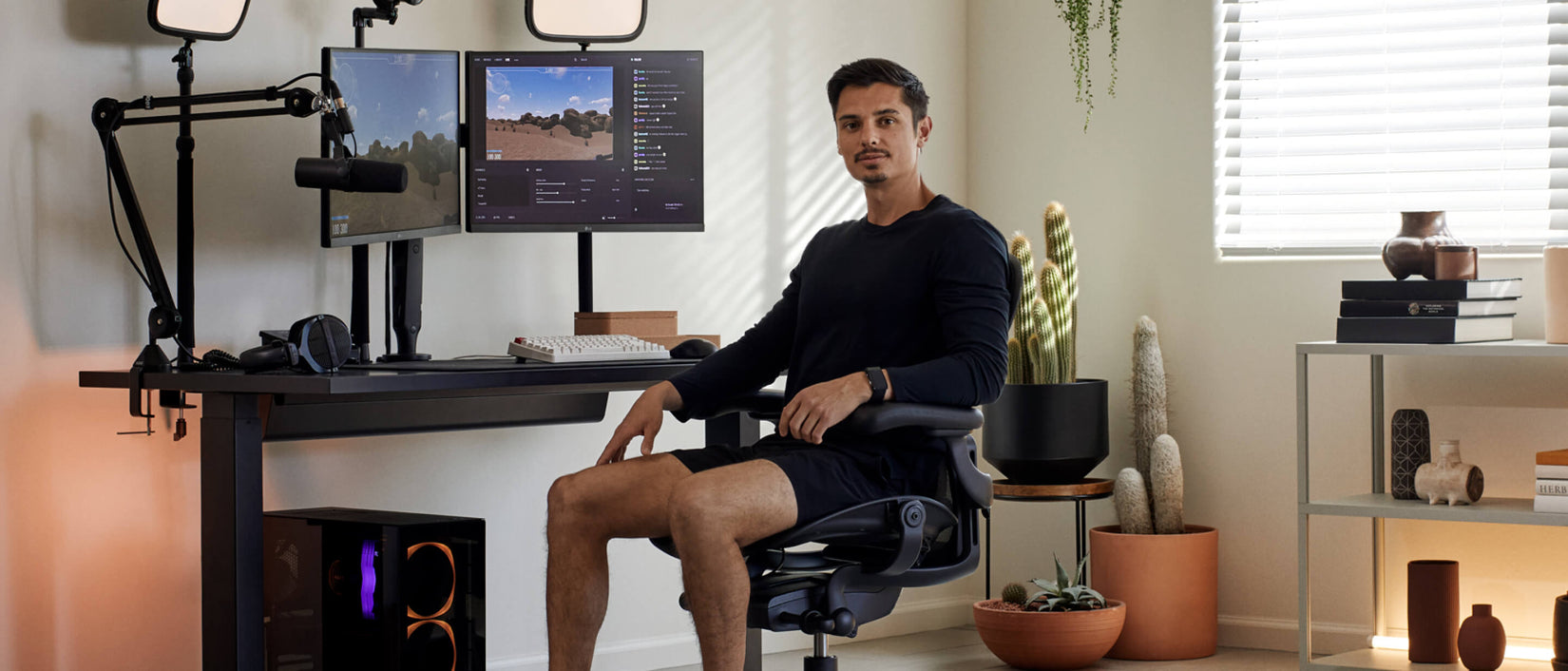 Foto van gamer Xaryu die voor de camera zit in een Aeron-gamingstoel in grafiet met achter hem een gamingopstelling met een Nevi-gamingtafel en Ollin-dubbele monitorarmen