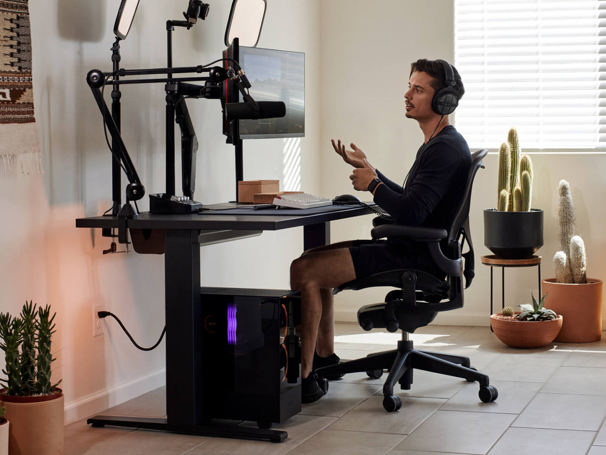 Gamer Xaryu zit aan zijn thuisgamingopstelling met een Aeron-gamingstoel in grafiet met een Nevi-gamingbureau en Ollin dubbele monitorarmen