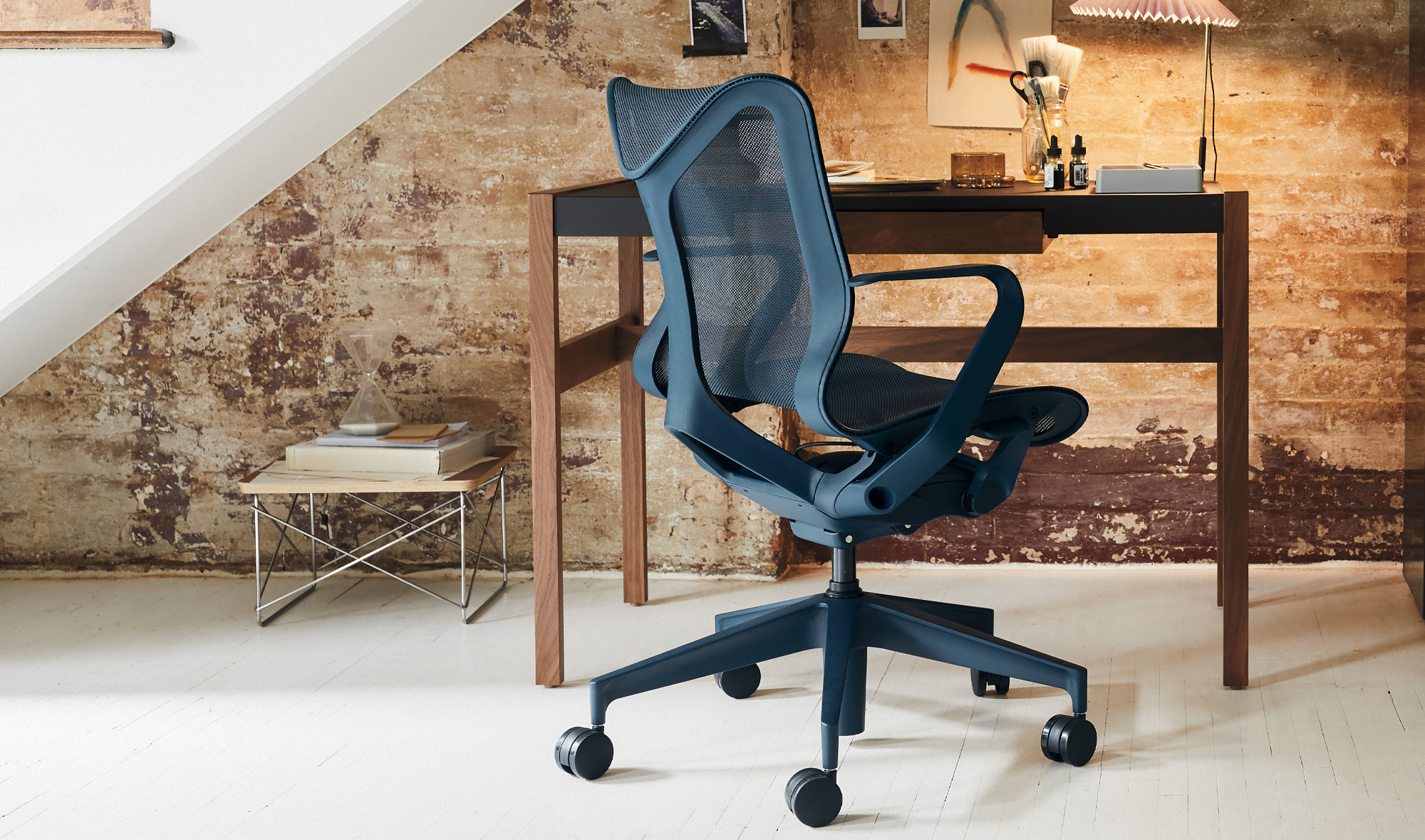 Een blauwe Herman Miller Cosm-bureaustoel staat voor een bureau en onder een trap in een huiselijke omgeving.