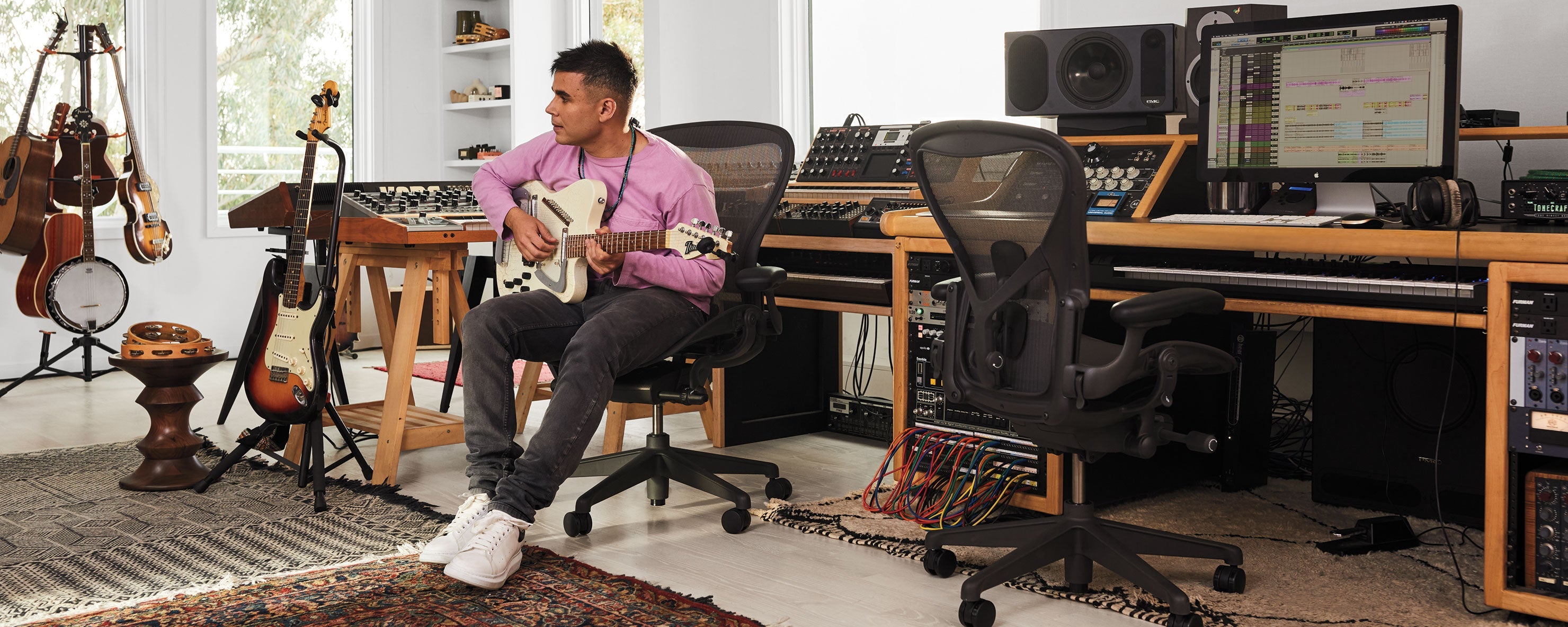 Foto van Rostam, muzikant, producer en componist, in zijn muziekstudio terwijl hij gitaar speelt, zittend in een Aeron-bureaustoel in grafiet