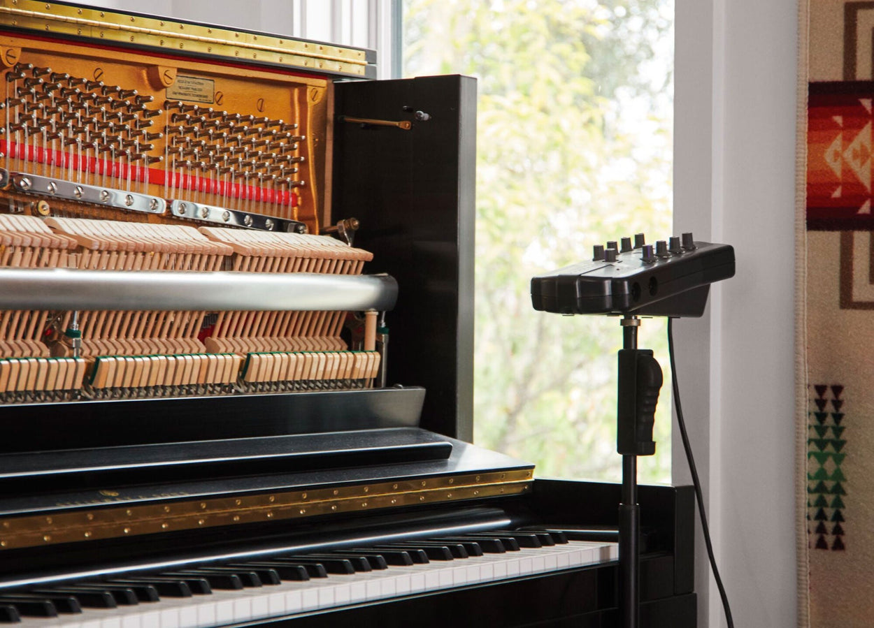 Een rechtopstaande piano met open voorkant en geluidsopnameapparatuur ernaast.